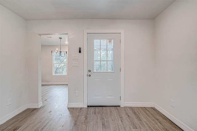 doorway featuring light wood-type flooring, a wealth of natural light, and a chandelier