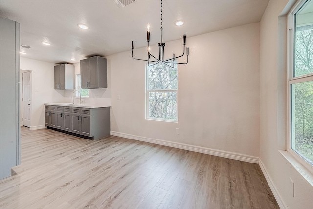 kitchen with gray cabinets, light hardwood / wood-style flooring, hanging light fixtures, and an inviting chandelier