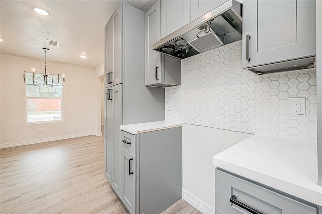 kitchen featuring gray cabinets, wall chimney exhaust hood, an inviting chandelier, and light hardwood / wood-style flooring