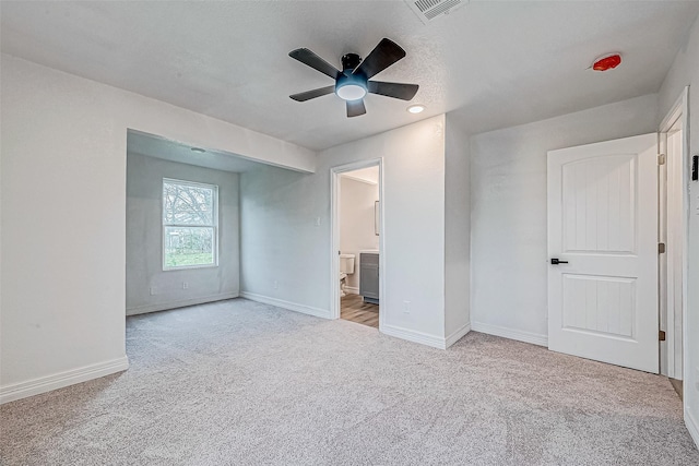 unfurnished bedroom featuring ensuite bath, ceiling fan, light colored carpet, and a textured ceiling