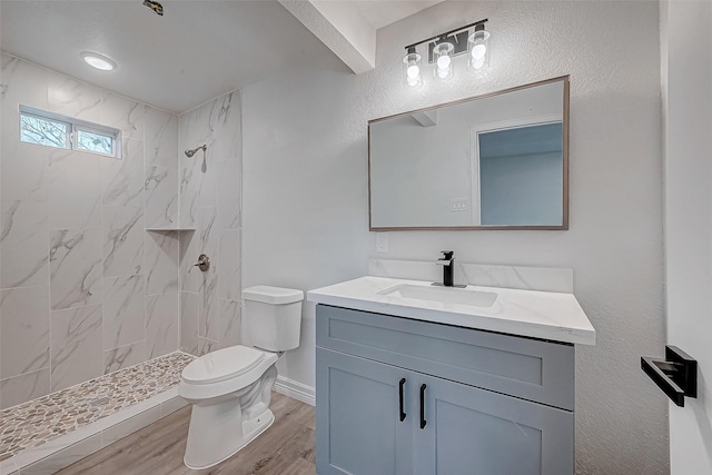 bathroom featuring hardwood / wood-style flooring, vanity, toilet, and tiled shower