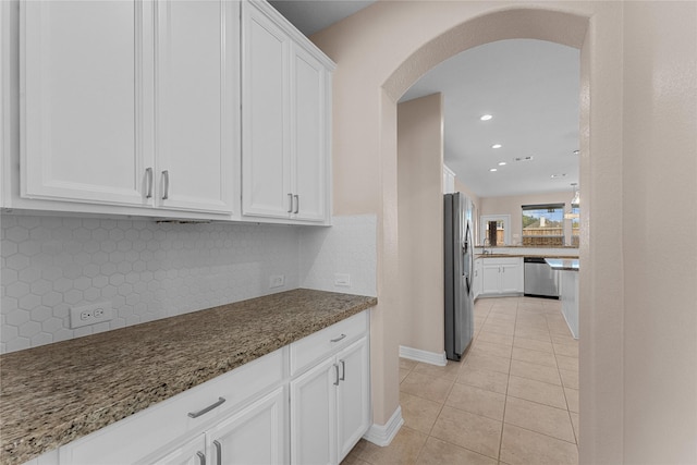 kitchen with light tile patterned flooring, tasteful backsplash, dark stone countertops, appliances with stainless steel finishes, and white cabinets