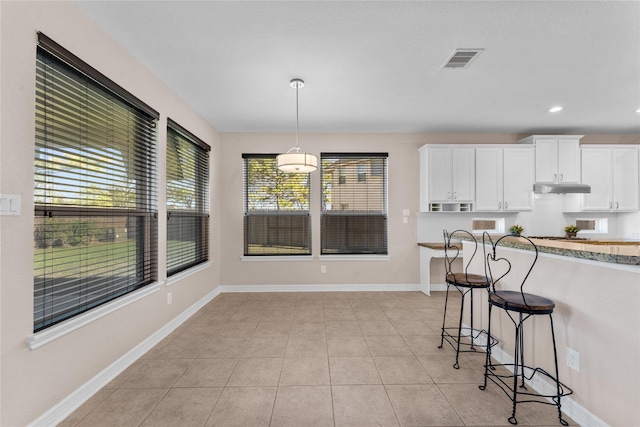 kitchen with hanging light fixtures, white cabinetry, light tile patterned floors, and a kitchen breakfast bar