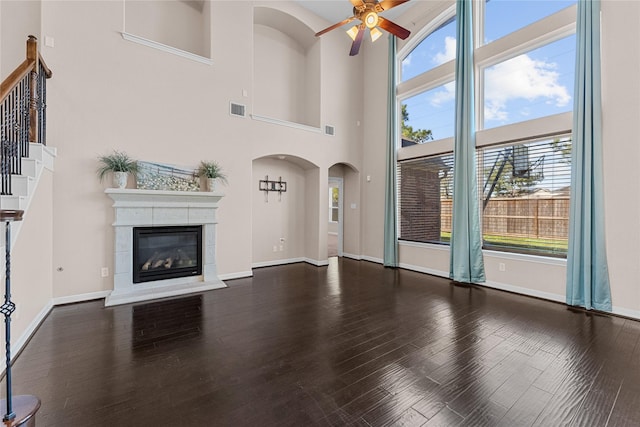 unfurnished living room with dark wood-type flooring, a tile fireplace, ceiling fan, and a high ceiling