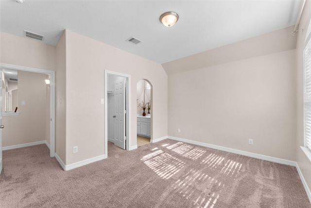 unfurnished bedroom with vaulted ceiling, a walk in closet, a closet, and light carpet