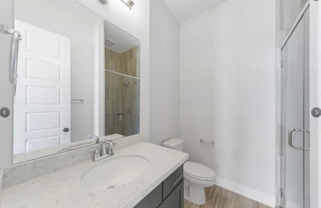 bathroom featuring vanity, toilet, wood-type flooring, and a shower with door