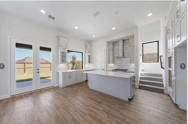 kitchen featuring a kitchen island, tasteful backsplash, wall chimney range hood, and french doors