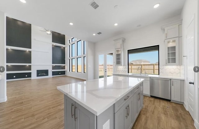 kitchen featuring light wood-type flooring, a center island, stainless steel dishwasher, and gray cabinetry