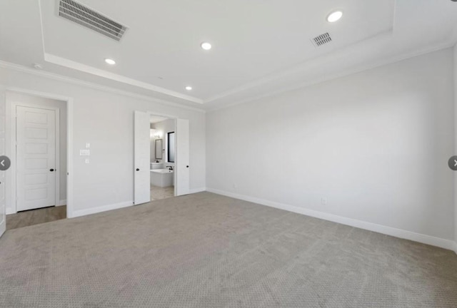 unfurnished bedroom featuring a raised ceiling, ensuite bath, crown molding, and light colored carpet