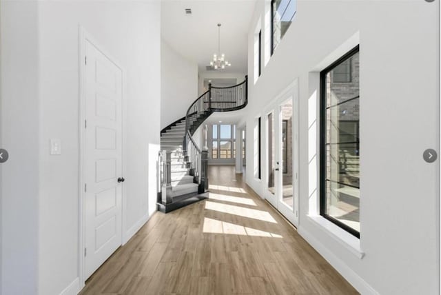 hallway with a chandelier, a towering ceiling, and light hardwood / wood-style flooring