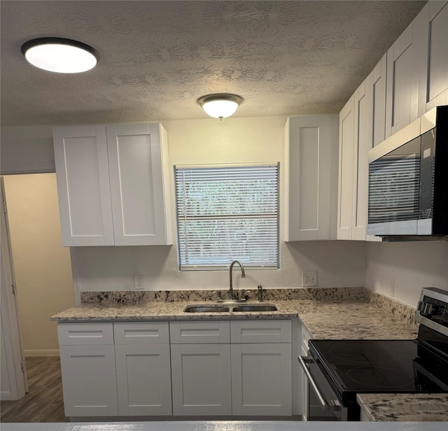 kitchen featuring light stone countertops, white cabinetry, sink, stainless steel appliances, and a textured ceiling