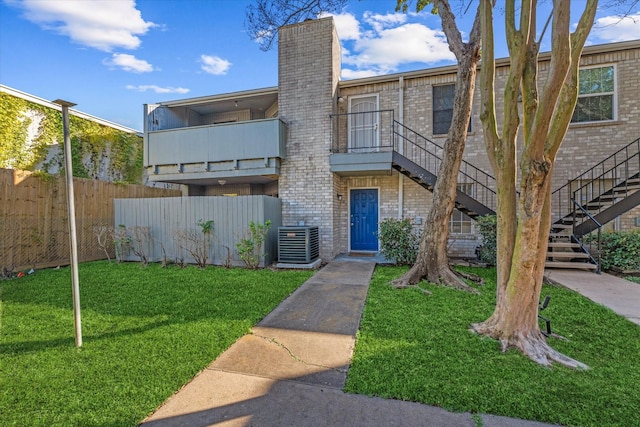 view of front of property with cooling unit, a balcony, and a front lawn