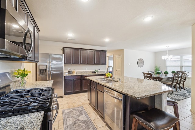 kitchen featuring sink, an island with sink, appliances with stainless steel finishes, a kitchen bar, and a chandelier