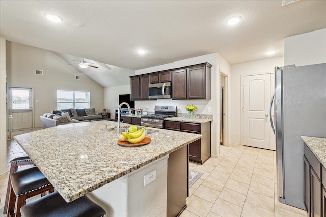 kitchen with light stone countertops, appliances with stainless steel finishes, vaulted ceiling, sink, and a center island with sink