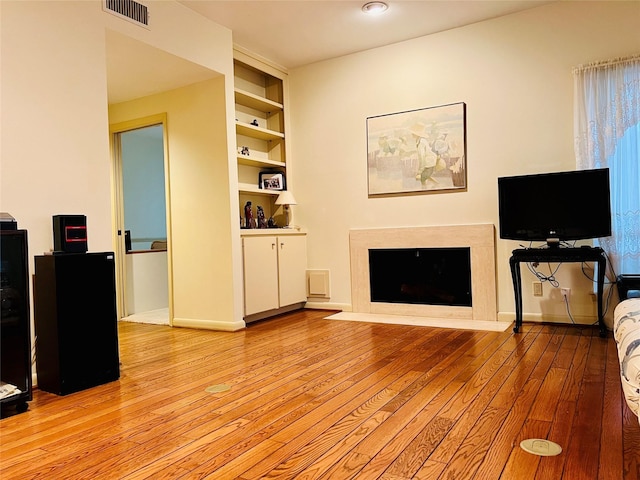 living room with built in features, a high end fireplace, and light hardwood / wood-style flooring