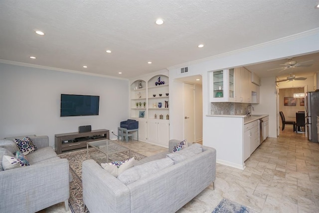 living room featuring built in shelves, ceiling fan, ornamental molding, and sink