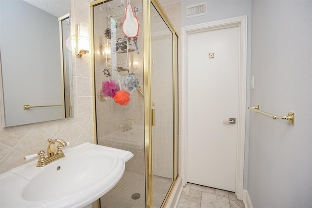 bathroom featuring a textured ceiling, backsplash, a shower with shower door, and sink