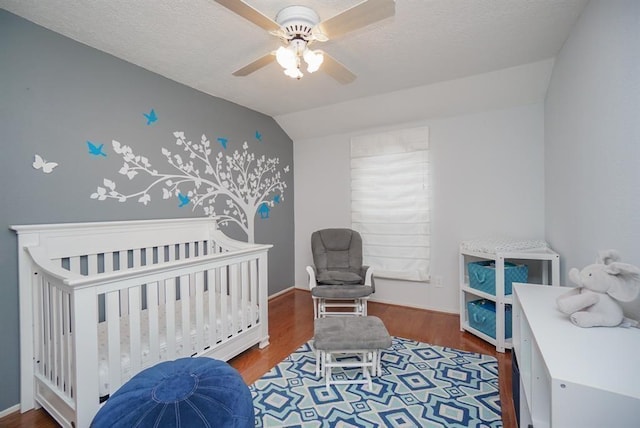 bedroom featuring hardwood / wood-style floors, ceiling fan, a crib, and vaulted ceiling