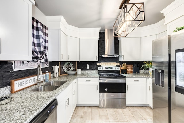 kitchen with light stone countertops, appliances with stainless steel finishes, wall chimney exhaust hood, sink, and white cabinetry