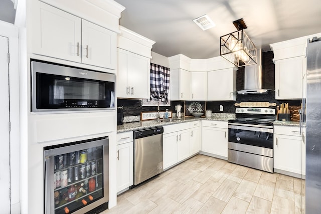 kitchen featuring white cabinetry, light stone countertops, wall chimney exhaust hood, beverage cooler, and appliances with stainless steel finishes