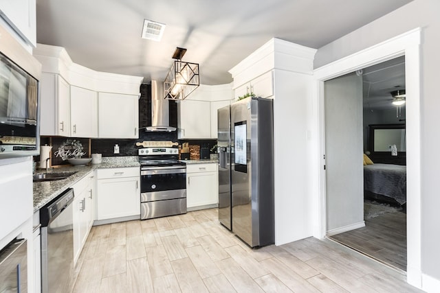 kitchen featuring light stone countertops, stainless steel appliances, wall chimney range hood, pendant lighting, and white cabinetry