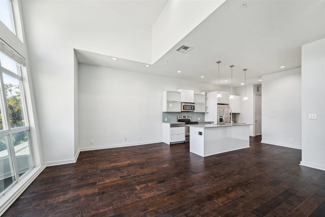 kitchen with white cabinetry, stainless steel appliances, dark wood-type flooring, pendant lighting, and a center island with sink