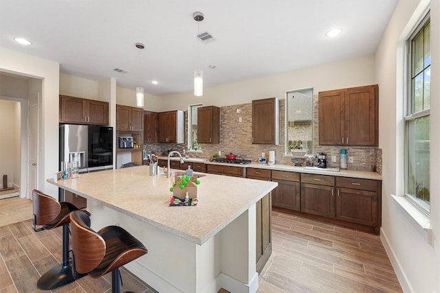 kitchen featuring stainless steel appliances, a kitchen breakfast bar, decorative light fixtures, decorative backsplash, and a center island with sink