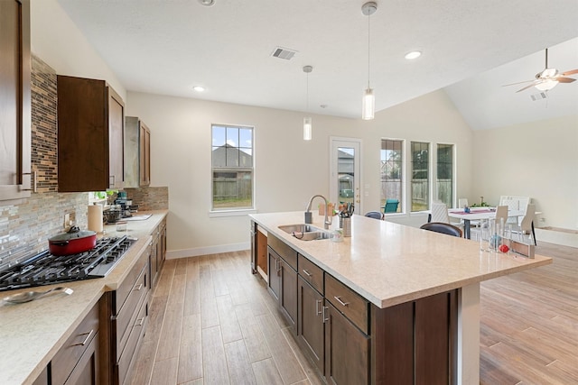 kitchen with pendant lighting, stainless steel gas stovetop, sink, light wood-type flooring, and an island with sink