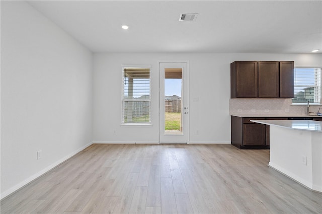kitchen with dark brown cabinets, visible vents, backsplash, light wood-style floors, and light countertops