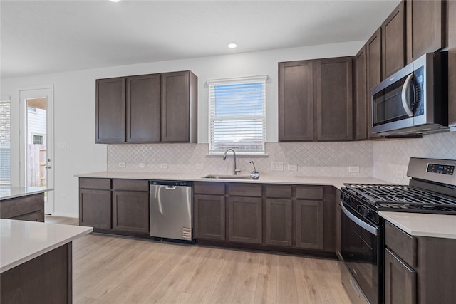 kitchen featuring light countertops, a sink, dark brown cabinetry, light wood-style flooring, and appliances with stainless steel finishes