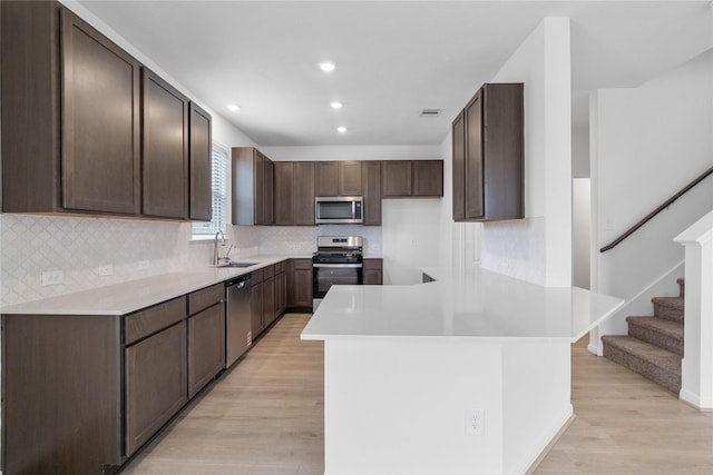 kitchen featuring light countertops, a sink, light wood-type flooring, a peninsula, and appliances with stainless steel finishes