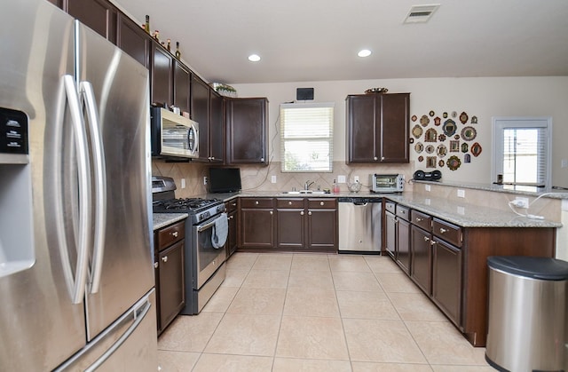 kitchen featuring kitchen peninsula, light stone countertops, plenty of natural light, and appliances with stainless steel finishes