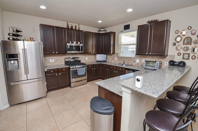 kitchen featuring sink, appliances with stainless steel finishes, dark brown cabinets, a kitchen bar, and kitchen peninsula