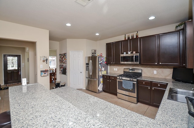 kitchen featuring decorative backsplash, dark brown cabinets, stainless steel appliances, and light tile patterned floors