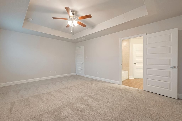 unfurnished bedroom with ceiling fan, a raised ceiling, light carpet, and ensuite bath