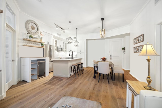 dining space featuring rail lighting, light hardwood / wood-style floors, crown molding, and sink