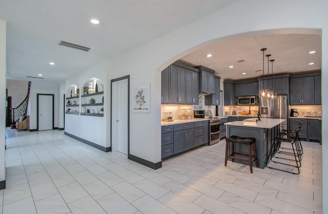 kitchen with stainless steel appliances, gray cabinets, hanging light fixtures, a breakfast bar area, and an island with sink