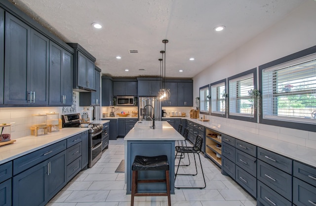 kitchen with a breakfast bar, stainless steel appliances, blue cabinets, decorative light fixtures, and an island with sink