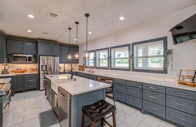 kitchen featuring sink, tasteful backsplash, decorative light fixtures, a center island with sink, and appliances with stainless steel finishes