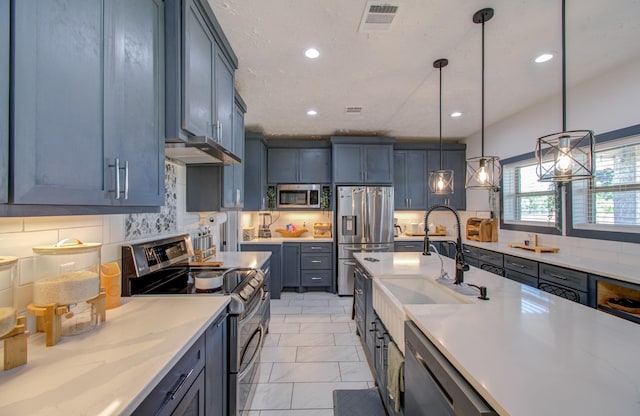 kitchen featuring sink, decorative backsplash, appliances with stainless steel finishes, decorative light fixtures, and light stone counters