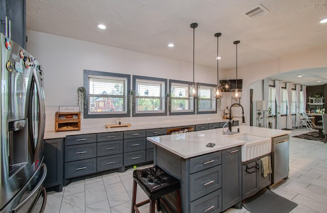 kitchen with a center island with sink, hanging light fixtures, sink, gray cabinets, and appliances with stainless steel finishes