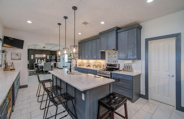 kitchen with a breakfast bar, electric range, sink, and an island with sink