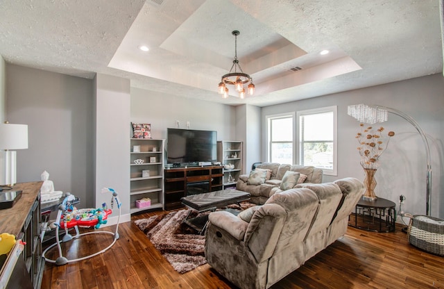 living room featuring a textured ceiling, a notable chandelier, dark wood-type flooring, and a tray ceiling