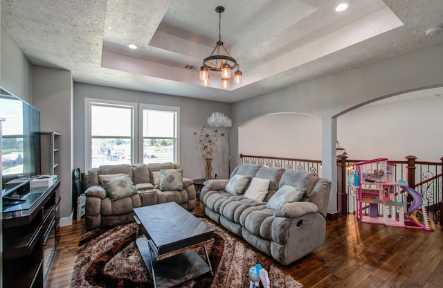 living room with dark hardwood / wood-style flooring, a tray ceiling, and a notable chandelier