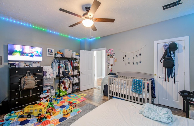 bedroom featuring hardwood / wood-style floors, a nursery area, a textured ceiling, and ceiling fan