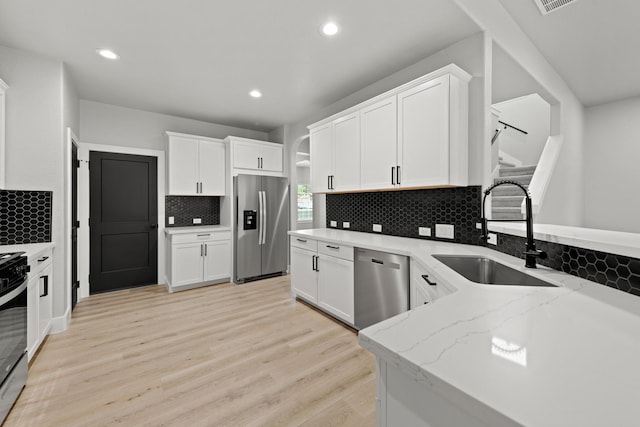 kitchen with sink, stainless steel appliances, light stone counters, white cabinets, and light wood-type flooring