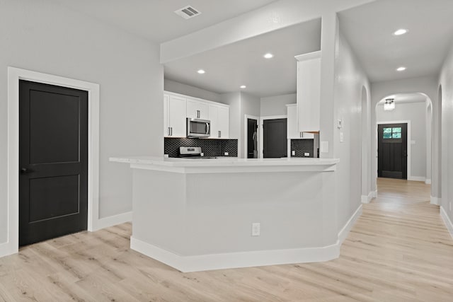 kitchen with stainless steel appliances, kitchen peninsula, decorative backsplash, white cabinets, and light wood-type flooring