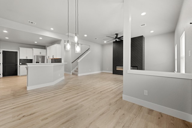 living room featuring ceiling fan, a large fireplace, and light wood-type flooring