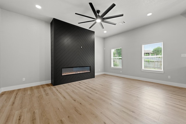 unfurnished living room featuring ceiling fan, a large fireplace, and light wood-type flooring