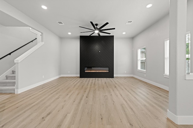 unfurnished living room with ceiling fan, a large fireplace, and light wood-type flooring